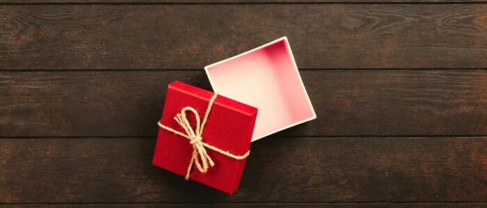 Top view of an open red gift box tied with twine on a wooden surface.